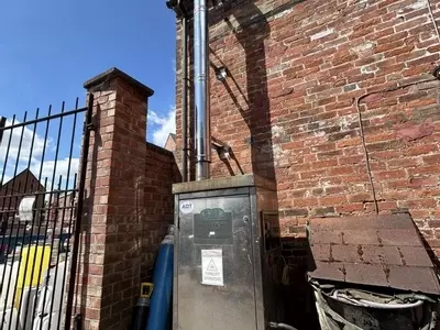 Nilfisk DTE static pressure washer fitted with a stainless steel flue extension at a brewery in Burton, installed to safely redirect boiler exhaust fumes away from a confined courtyard cleaning area.